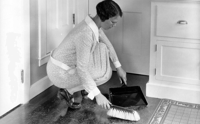 Schwarz/Weiß-Foto: Frau fegt mit Handfeger und Kehrblech den Küchenboden.