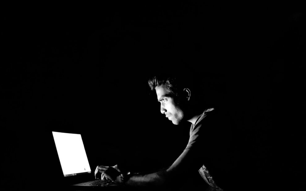 Mann am Laptop sitzt im Dunkeln