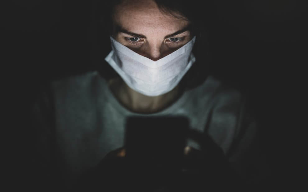 Mann im Dunkeln mit Gesichtsmaske am Handy