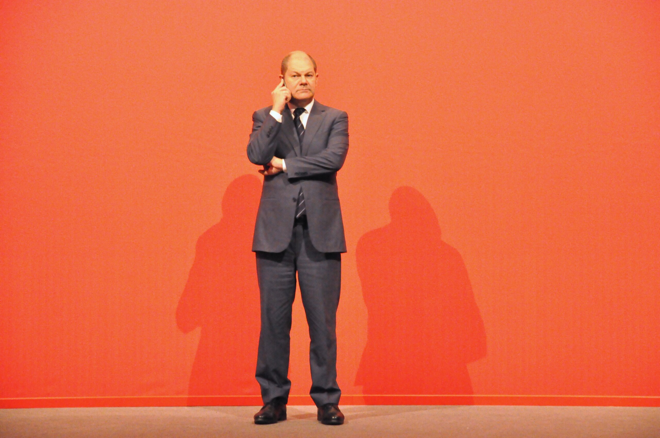 Olaf Scholz steht vor einer roten Wand und telefoniert